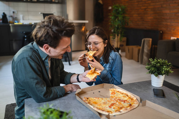 Young couple caucasian man and woman modern husband and wife eat pizza at home male and female friends having time together with food domestic life concept real people copy space selective focus - Φωτογραφία, εικόνα