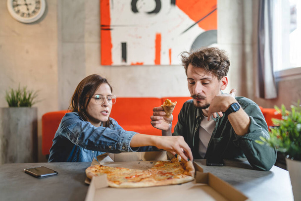 Young couple caucasian man and woman modern husband and wife eat pizza at home male and female friends having time together with food domestic life concept real people copy space selective focus - Foto, afbeelding