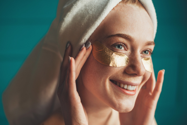 Woman applying golden patches under her eyes, taking care her facial skin. Beauty treatment. Beauty routine. - Foto, Bild