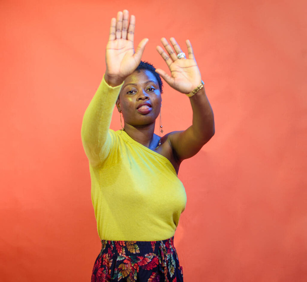Studio picture of a dancing African Nigerian lady or woman wearing a yellow top with a low cut hairstyle on her head - Fotó, kép