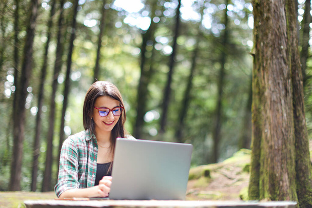 Young latin woman sitting in the forest working with laptop freelancing smiling at Costa Rica. High quality photo - Photo, Image