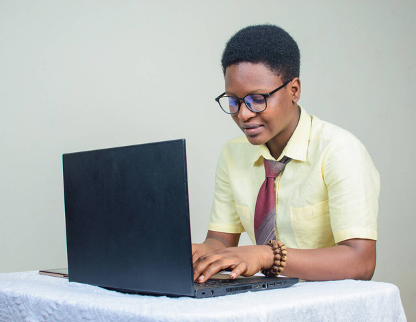 Happy Female African with glasses and beads on her wrist, using laptop or computer by typing on the keyboard - Photo, image