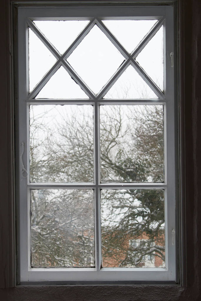 Lähikuva lasi-ikkuna sisältä, katselee ulos kylmällä säällä aamulla. Puinen ikkunalasi huonolla eristyksellä, suljettu ja suljettu näkymä talvikohtaukseen lumella, pakkasella ja jäällä - Valokuva, kuva