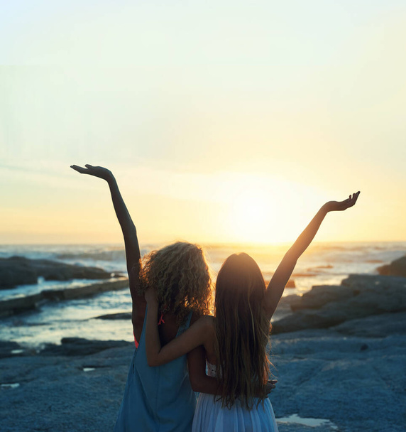 two woman friends on beach celebrating with arms raised looking at sunset enjoying travel freedom lifestyle. - 写真・画像