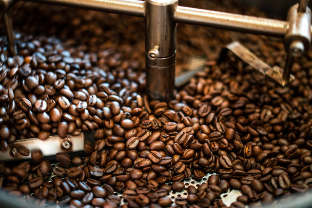 Φρεσκοψημένοι αρωματικοί κόκκοι καφέ πάνω από μια σύγχρονη μηχανή ψησίματος καφέ - Φωτογραφία, εικόνα