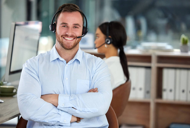 Finding answers is what were best at. Portrait of a confident young man using a headset in a modern office with his colleague working in the background - Foto, Imagem