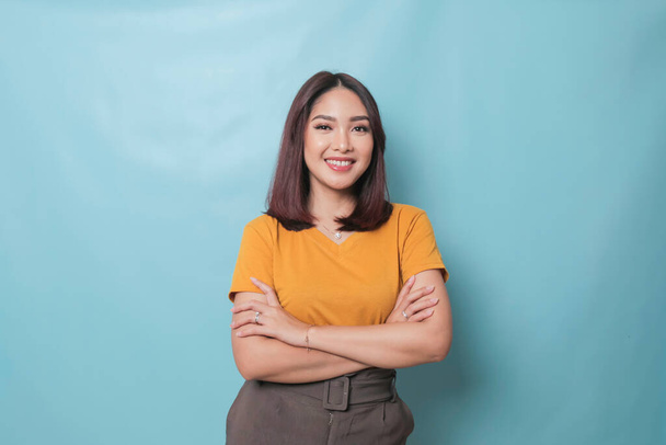 Portrait of a confident smiling girl standing with arms folded and looking at camera isolated over blue background - Photo, Image