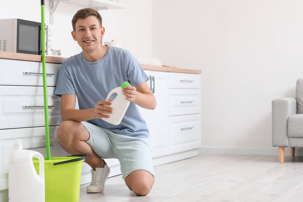Young man with bottle of detergent in kitchen - Foto, Bild