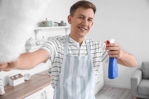 Młody człowiek z detergentem i szczotką do kurzu w kuchni - Zdjęcie, obraz