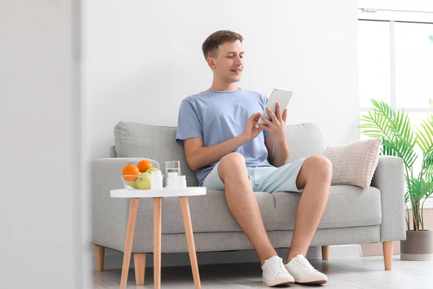Young man using tablet computer on sofa at home - Foto, afbeelding