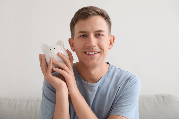Young man holding piggy bank at home - Foto, imagen