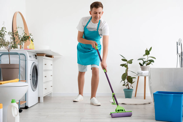 Young man mopping floor in modern bathroom - Foto, afbeelding