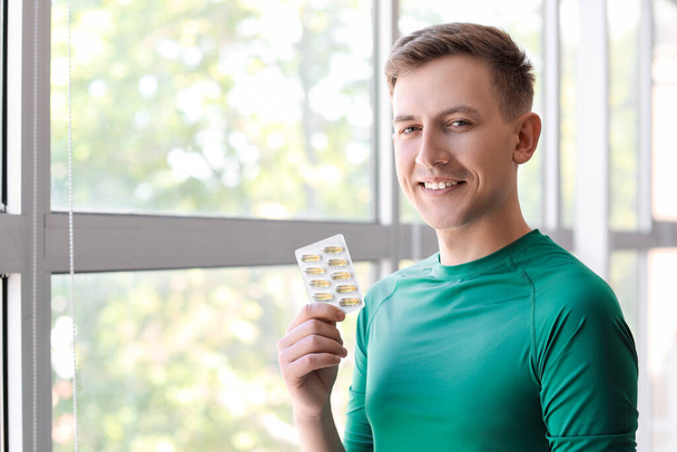 Young man with blister of pills near window - Fotografie, Obrázek
