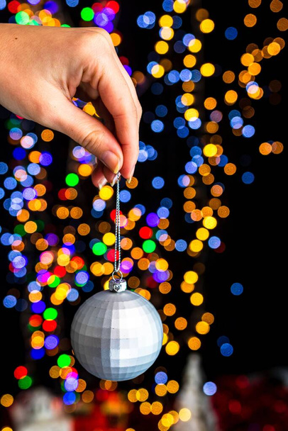 A vertical shot of a hand holding a Christmas white ball decoration with bokeh Christmas lights - Foto, immagini