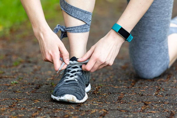 A closeup shot of a Young woman makes fitness and ties shoelaces in nature with a smartwatch on her arm - Foto, imagen
