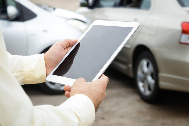 Auto insurance concept. A man, a company officer holding a tablet, takes pictures and records the accident car to inform the insurance company. - Photo, image