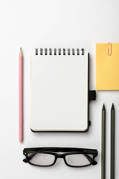 A closeup of a white desk with office supplies, a notebook, pencils and sticky notes - Foto, afbeelding