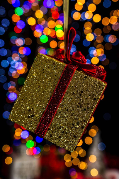 A vertical shot of a Christmas present wrapped in golden with red ribbon with bokeh lights in the background - Foto, Imagen
