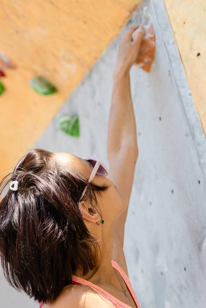 Спортивна жінка скелелазіння рухається вгору по крутій скелі, сходження на штучну стіну. Концепція екстремальних видів спорту та боулдингу
 - Фото, зображення