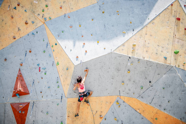 Sportswoman climber moving up on steep rock, climbing on artificial wall. Extreme sports and bouldering concept - Foto, Imagen