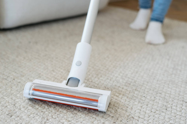 Ausgeschnittene Ansicht einer Person, die zu Hause einen drahtlosen Staubsauger benutzt. Konzept der Sauberkeit. Nutzung von Haushaltsgeräten. Hausfrauenarbeit. Reinigungsservice - Foto, Bild