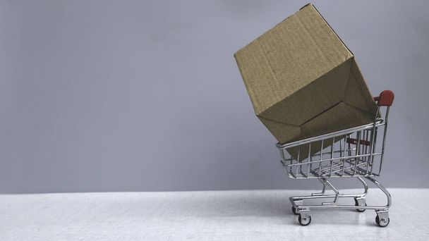 Shopping concept. A shopping cart with a large brown box in it on grey background with copy space. - Foto, Imagen