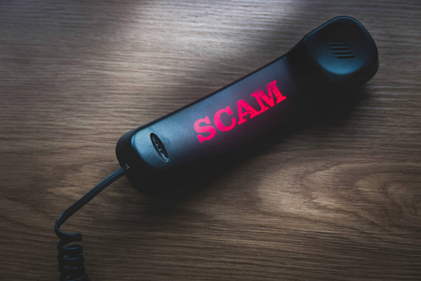 Call-Scam-Konzept. Selektiver Fokus des schwarzen Telefons mit einem verschwommenen und leuchtenden Text von Scam auf hölzernem Hintergrund. - Foto, Bild