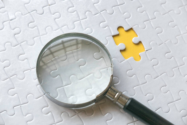 Selective focus of magnifying glass cone and an empty space of white jigsaw puzzle with yellow background. - Foto, immagini