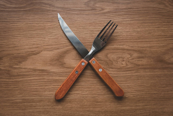 Yemek konsepti. Kesişen bıçağın üst görüntüsü, tahta masada kaşık.. - Fotoğraf, Görsel