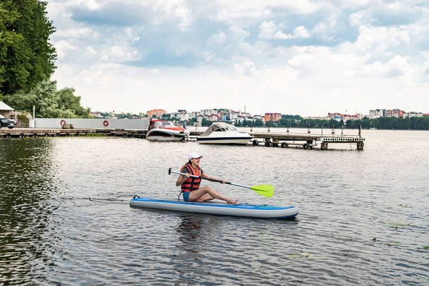 Charmant lächelnde Frau fährt mit dem Paddelbrett um den Stadtsee, aktiver Lebensstil, Sport und Gesundheit - Foto, Bild
