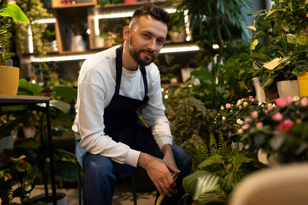jardinero masculino experimentado rodeado de plantas en maceta mirando a la cámara. - Foto, imagen