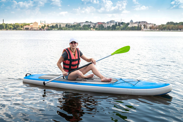 mujer bastante delgada flota en sup board y paleta larga en el lago de la ciudad. libertad, concepto de estilo de vida activo - Foto, Imagen