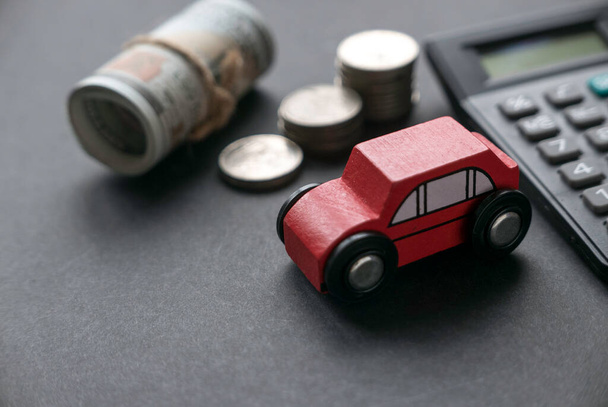 A red toy car together with coins, money and calculator on a black background. - Fotoğraf, Görsel