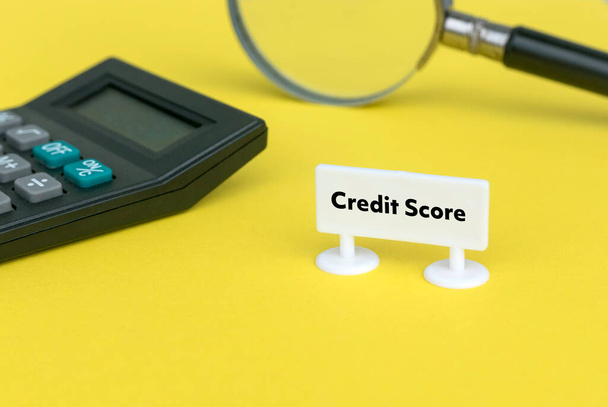 Selective focus of magnifying glass, calculator and white sign board written with Credit Score on yellow background. - Foto, afbeelding