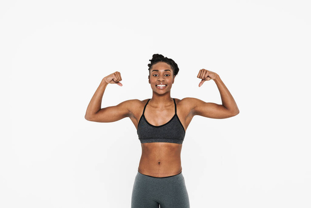 Young black sportswoman smiling and looking showing her biceps isolated over white background - Zdjęcie, obraz