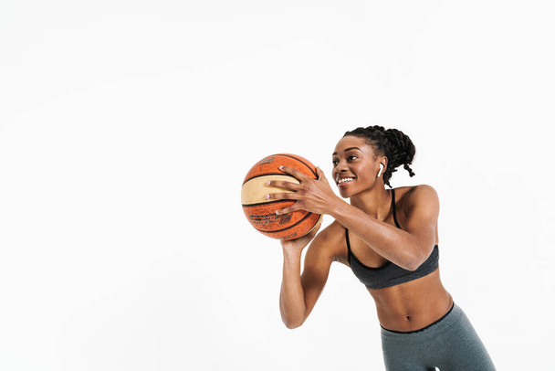 Black young sportswoman in earphones working out with basketball isolated over white background - Foto, Imagen