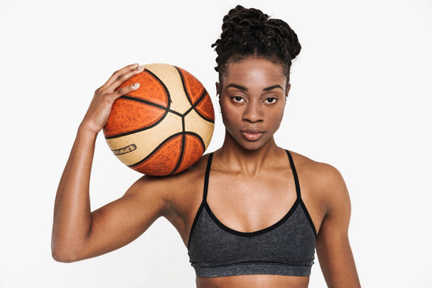 Black young sportswoman in earphones posing with basketball isolated over white background - Фото, изображение