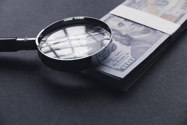 Selective focus of magnifying glass and money on a black background. - Valokuva, kuva