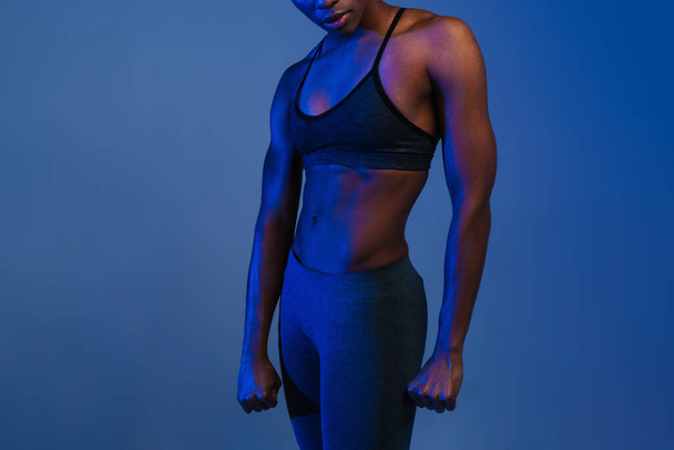 Black athletic woman in sportswear posing on camera isolated over blue background - Фото, изображение