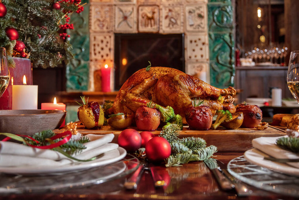 Stuffed fried chicken with broccoli, apple, rosemary, walnuts, tomatoes lying on a wooden board surrounded by a festive table, plates, glasses and Christmas tree decorations - Foto, Bild