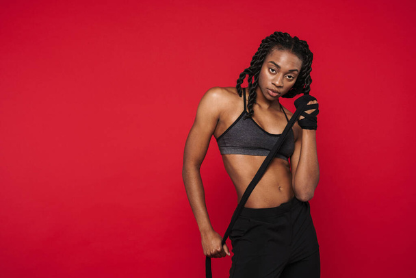 Young black sportswoman wearing bra posing with rope isolated over red background - Zdjęcie, obraz