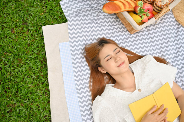 Draufsicht, Schöne und attraktive junge Asiatin legt sich mit ihrem Lieblingsbuch auf ihre Picknickdecke. Picknick-Konzept - Foto, Bild