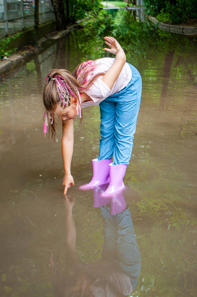 A happy braided girl in rubber boots is playing in muddy puddles. - Foto, Imagem
