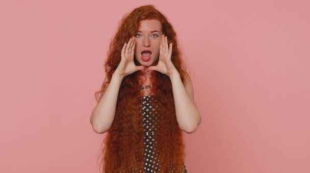 Εκφραστική γυναίκα κρατώντας το χέρι κοντά στο στόμα δυνατά ουρλιάζοντας, φωνάζοντας, φωνάζοντας, ανακοινώνει εκπτώσεις πώληση Γρήγορα, καλωσορίζει κάποιον γεια. Νεαρή κοκκινομάλλα κοπέλα απομονωμένη σε ροζ φόντο στούντιο - Φωτογραφία, εικόνα