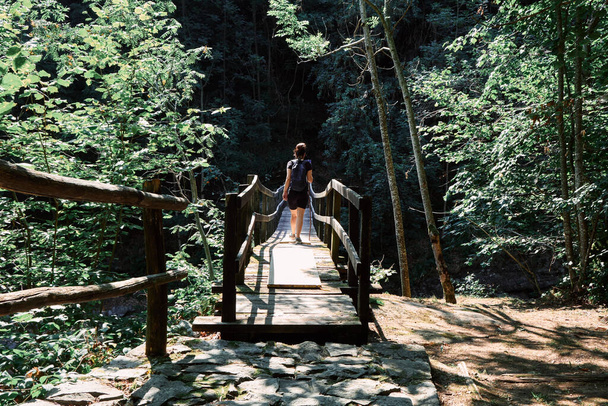 Woman tourist walks or hiking on a suspension wooden bridge on nature in the forest - 写真・画像