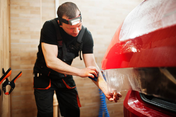 Car service worker put anti gravel film on a red car body at the detailing vehicle workshop. Car protection with special films. - Photo, image