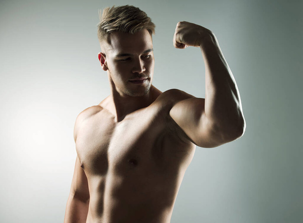 Do daily what others do occasionally. Studio shot of a muscular young man flexing his arm against a grey background - Zdjęcie, obraz
