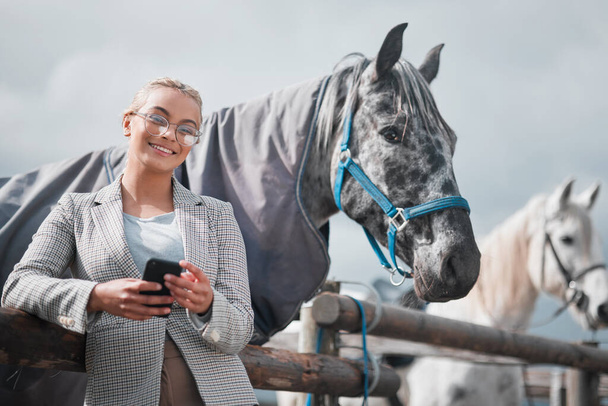 Fresh air and back rides. Portrait of an attractive woman using her cellphone while posing with a horse in an enclosed pasture on a farm - Zdjęcie, obraz