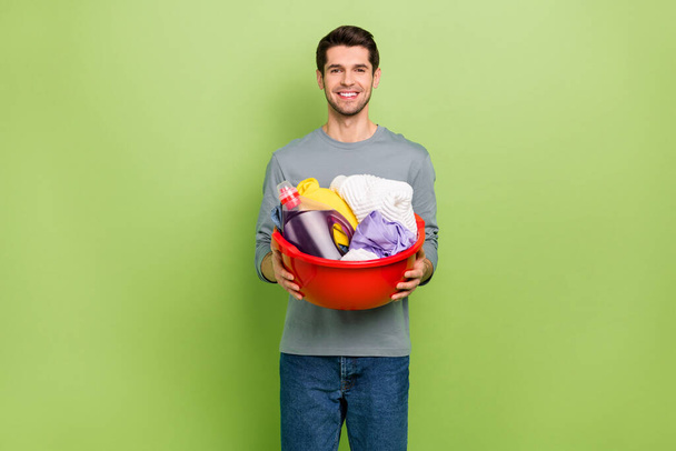 Photo of good mood cheerful man doing household chores cleaning dirty clothes isolated on green color background. - 写真・画像