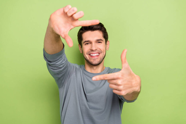 Photo of nice millennial brunet guy make photo wear grey pullover isolated on green color background. - Zdjęcie, obraz